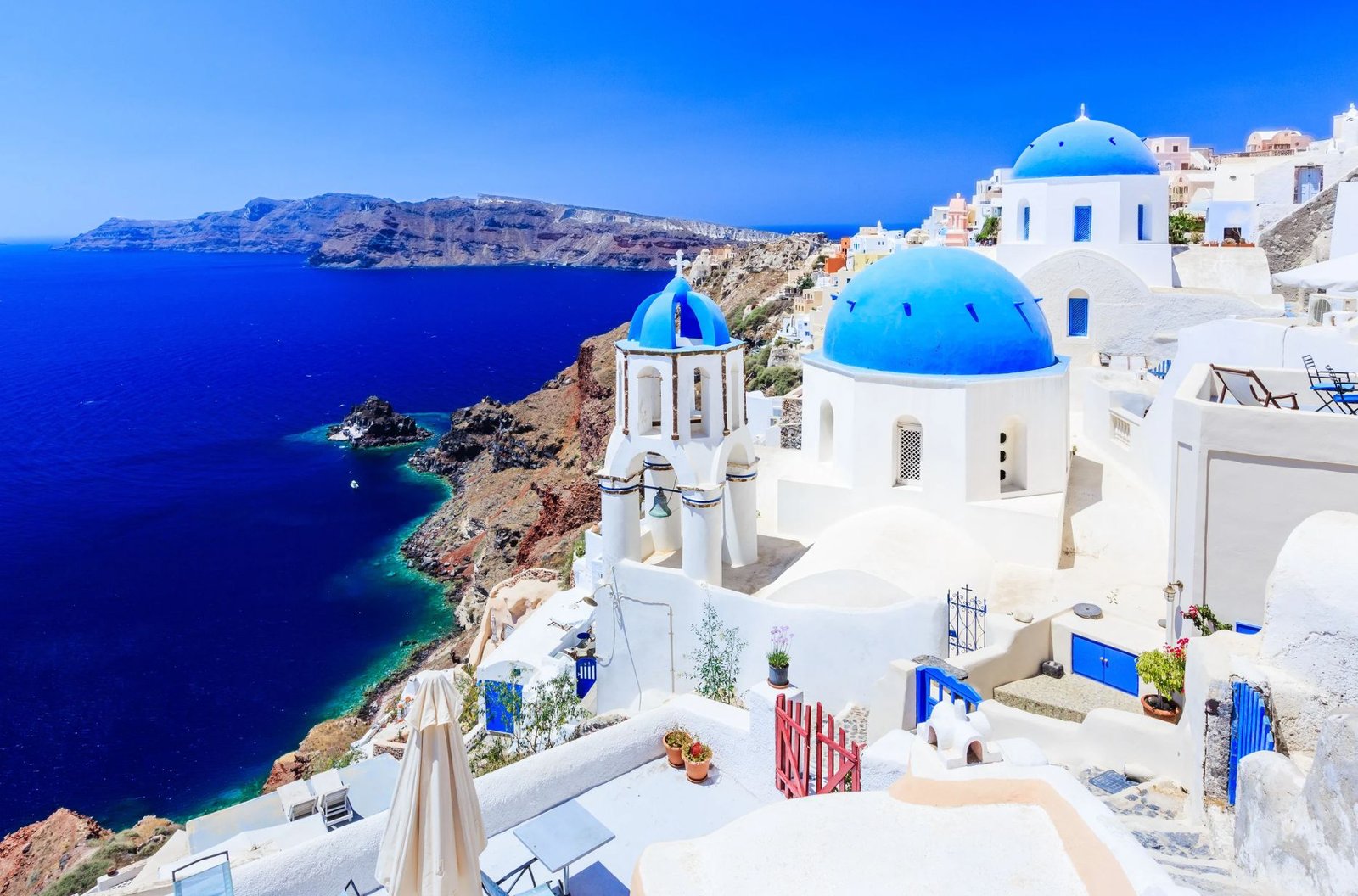 A Scenic View Of Santorini, Greece, Showcasing Its Iconic White Buildings And Blue Domes Against A Clear Sky